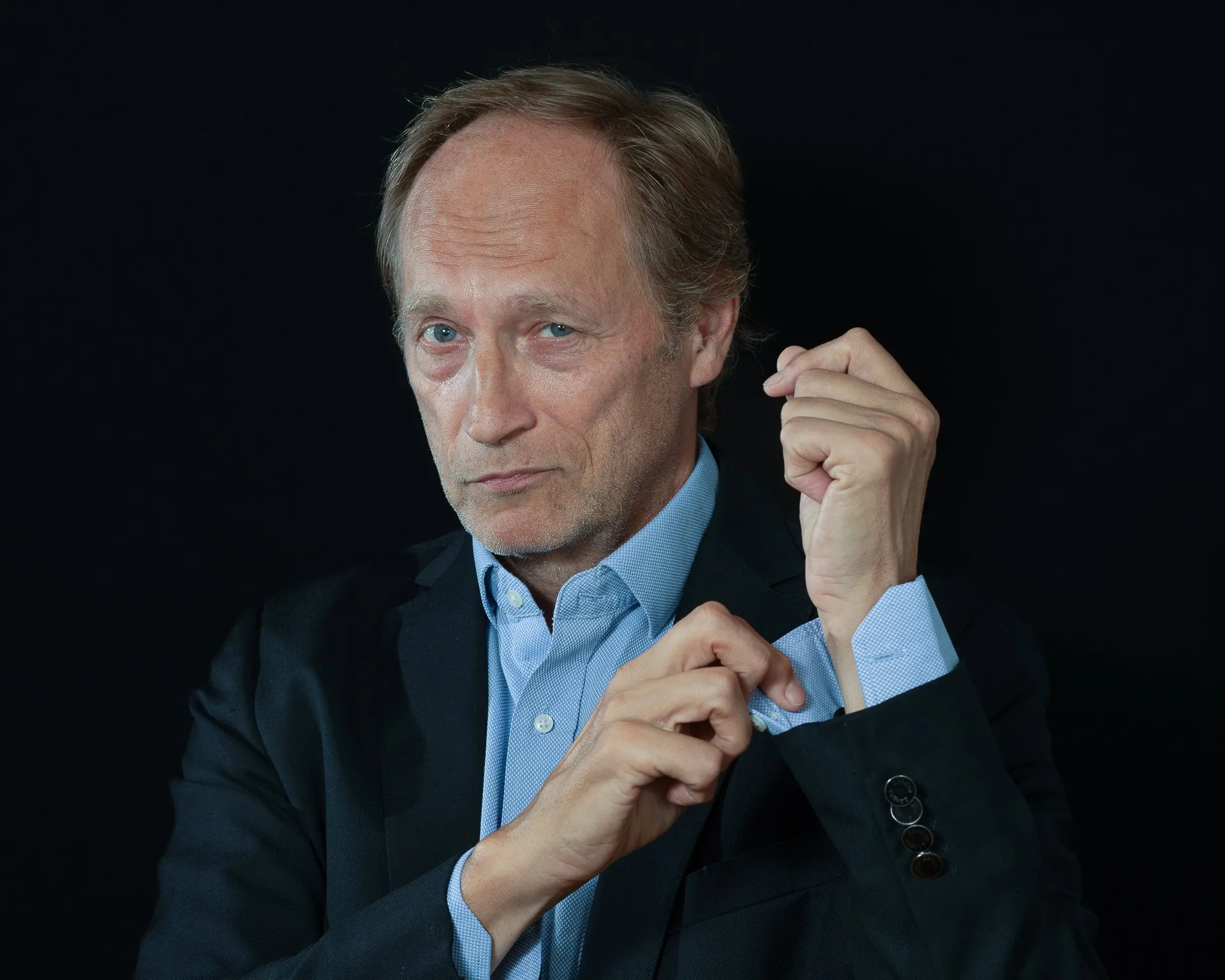 Janne Oravisto korjaa paidan kalvosinta tumman taustan edessä