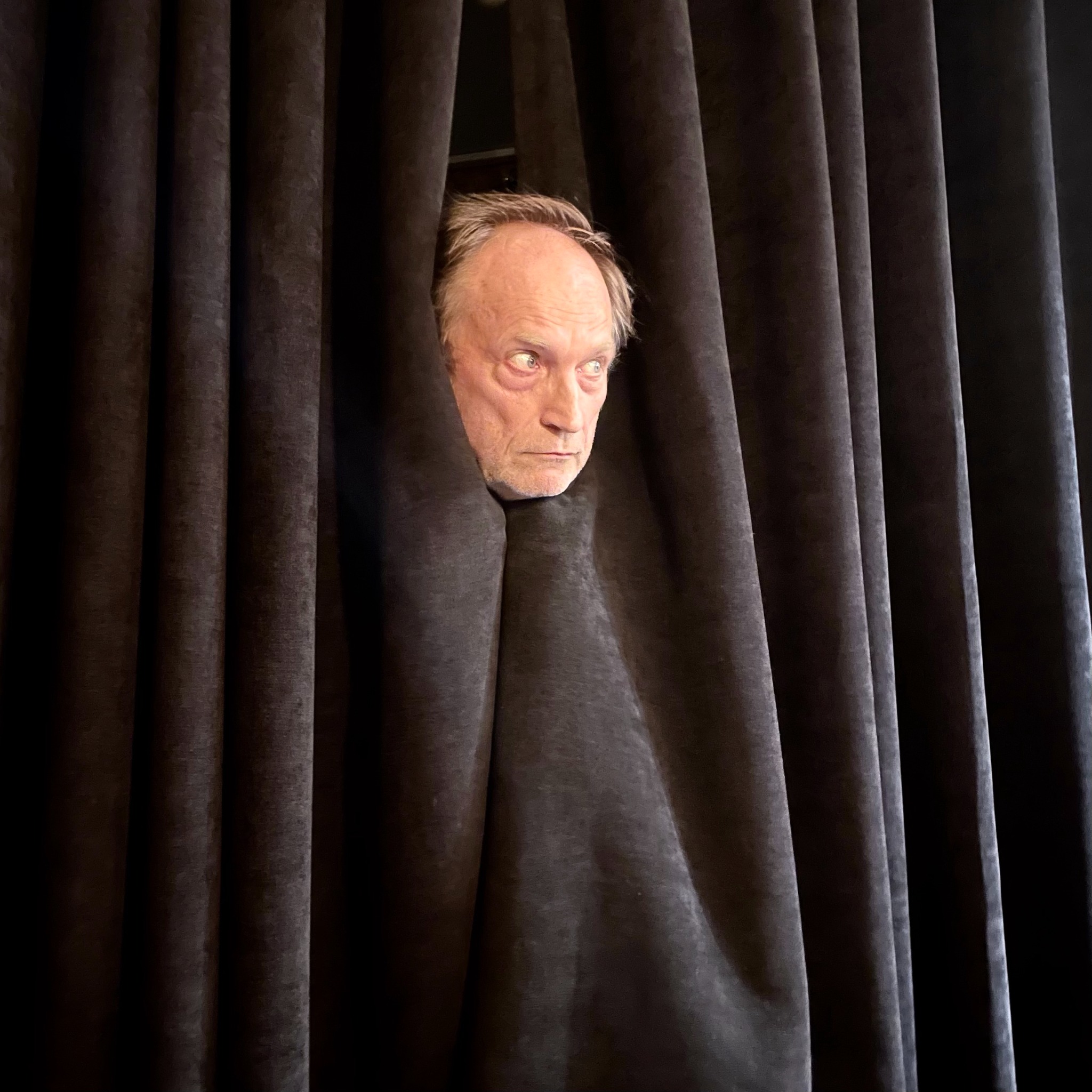 Janne Oravisto kurkistaa tummien teatteriverhojen välistä